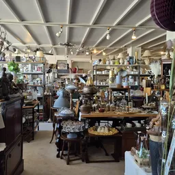 Overzicht van kringloopwinkel met diverse meubels, lampen, servies en huishoudartikelen op stellingen en tafels onder verlich