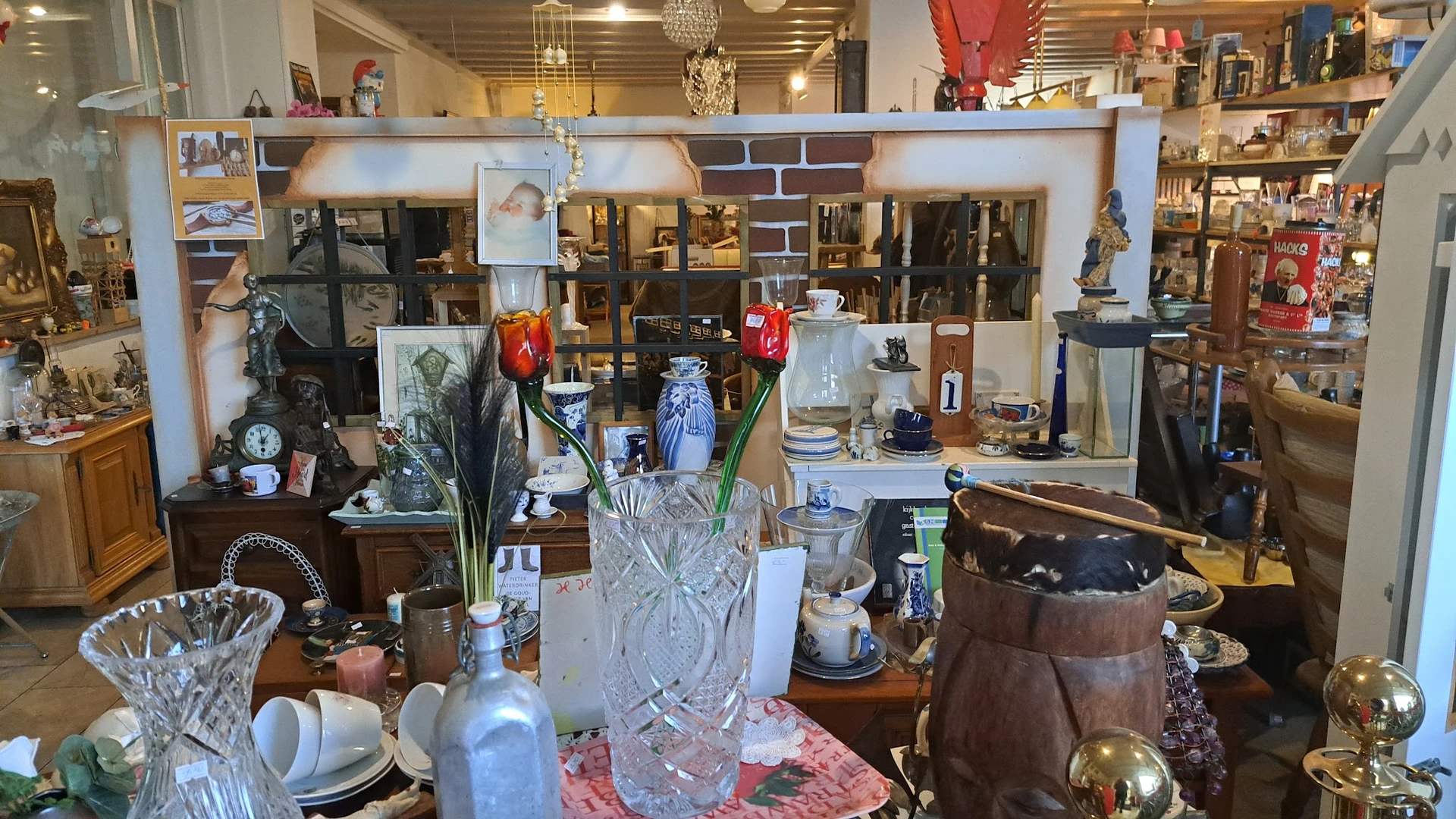 Verzameling huishoudelijke items en decorstukken op tafel en in kasten: kristallen vazen, servies, lampen en overig interieur