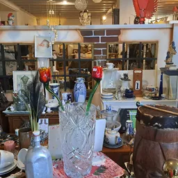 Verzameling huishoudelijke items en decorstukken op tafel en in kasten: kristallen vazen, servies, lampen en overig interieur