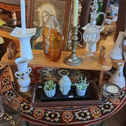 Vitrinekast met decoratieve objecten: witte vazen, plantjes in potten, en glazen items op zwarte achtergrond