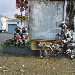 Decoratieve robot-figuren op een gele aanhanger naast de winkel, met winkellogo Primula zichtbaar