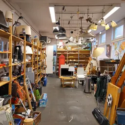 Winkelvloer van kringloopwinkel met gele stellingen vol huishoudelijke artikelen, lampen en diversen spullen