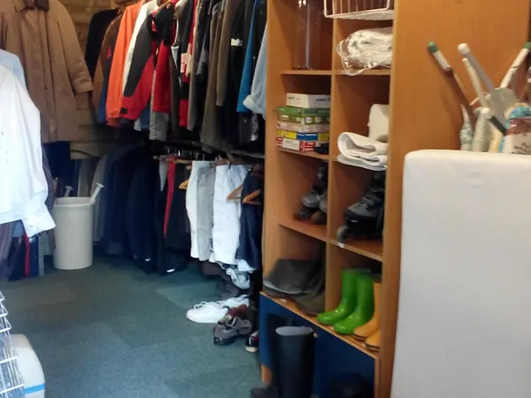 Kringloopwinkel interieur met kledingrekken, houten kasten en diverse items op de grond