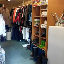 Kringloopwinkel interieur met kledingrekken, houten kasten en diverse items op de grond