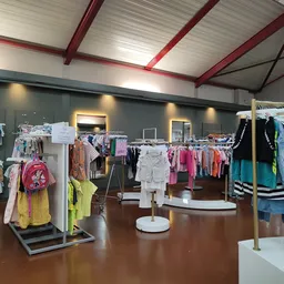 Winkelvloer van kringloopwinkel met rekken vol kinderkleding en speelgoed, moderne inrichting met rode balken in het plafond