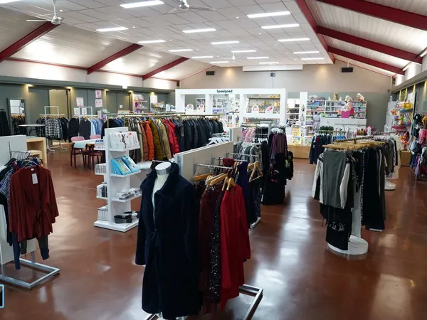 Winkelvloer van kringloopwinkel met rekken tweedehands kleding, verlichte plafonds en winkelafdelingen