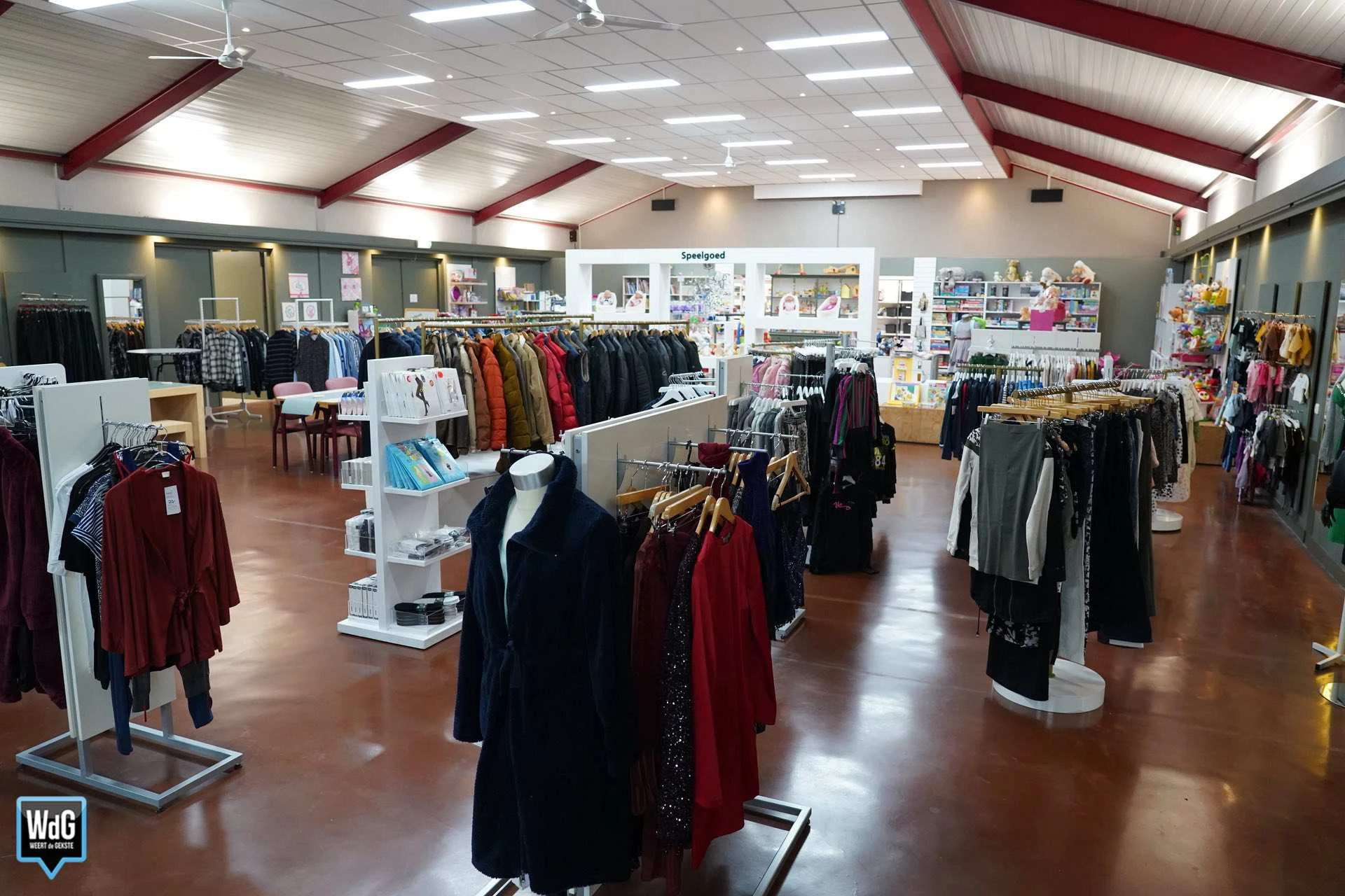 Winkelvloer van kringloopwinkel met rekken tweedehands kleding, verlichte plafonds en winkelafdelingen