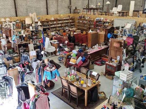 Overzicht van kringloopwinkel met kledingrekken, meubels, boeken en spullen verspreid over de vloer