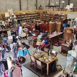 Overzicht van kringloopwinkel met kledingrekken, meubels, boeken en spullen verspreid over de vloer