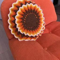 Gehaakte zonnebloem-kussen in oranje, geel en bruin op een rood corduroy fauteuil