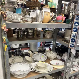 Metalen stellingkast met servies, porselein, schalen en andere huishoudartikelen op verschillende niveaus