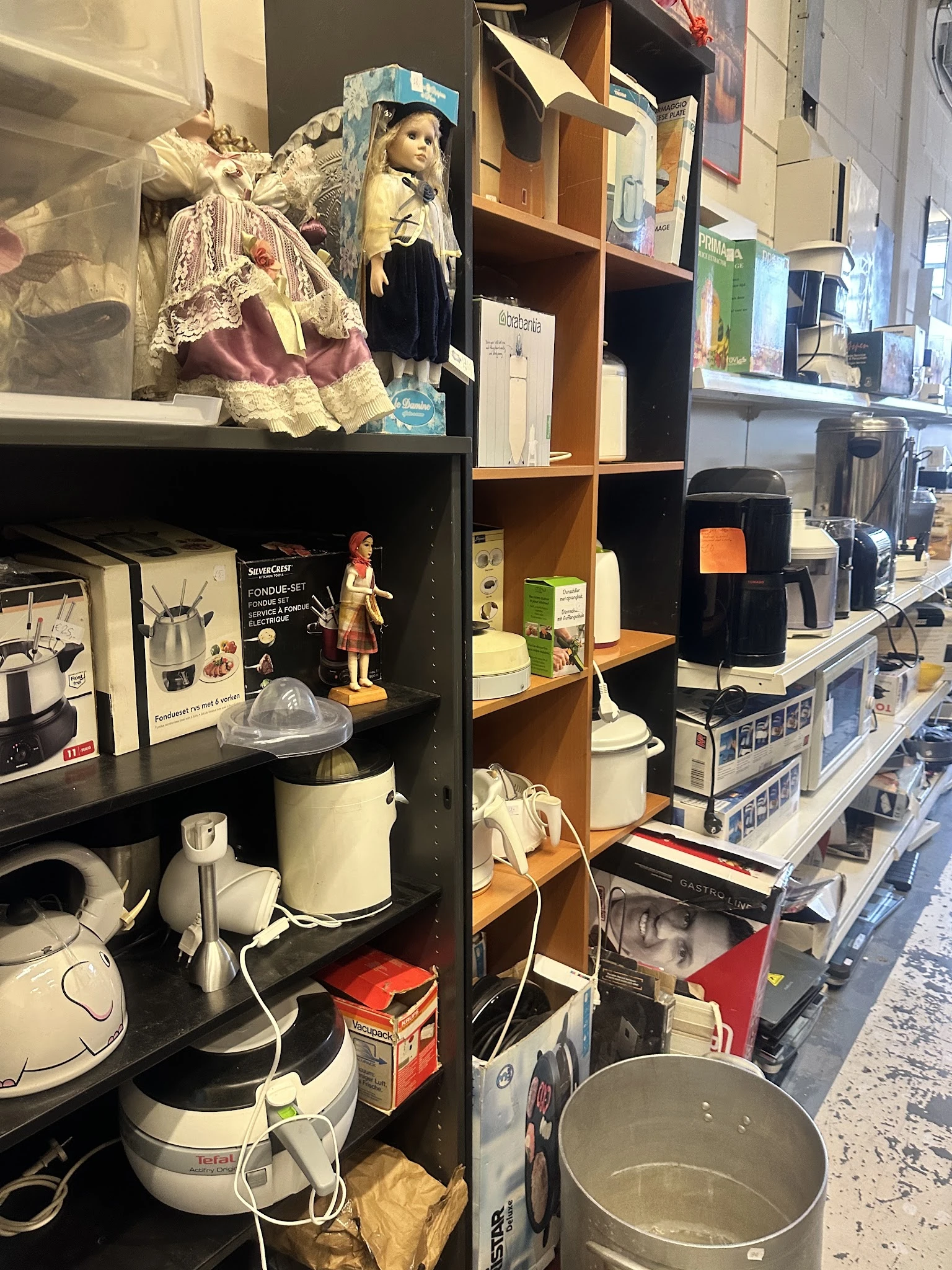 Stellingen met huishoudelijke apparaten en keukengerei, waaronder een waterkoker, koffiezetapparaat en diverse andere items i