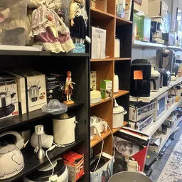 Stellingen met huishoudelijke apparaten en keukengerei, waaronder een waterkoker, koffiezetapparaat en diverse andere items i