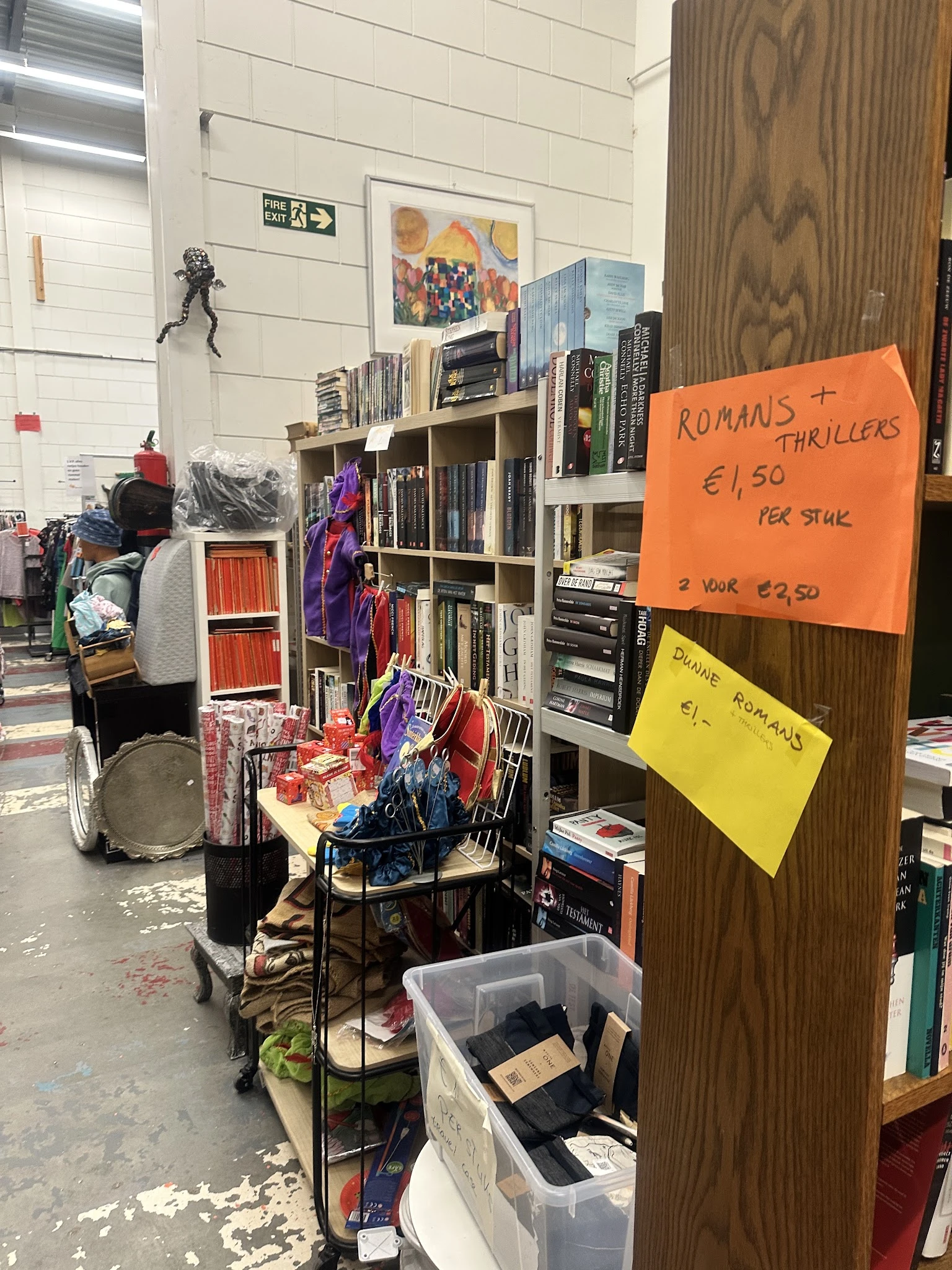 Boekenkasten met tweedehands boeken en prijs­kaarten met aanbiedingen, in een kringloopwinkel.