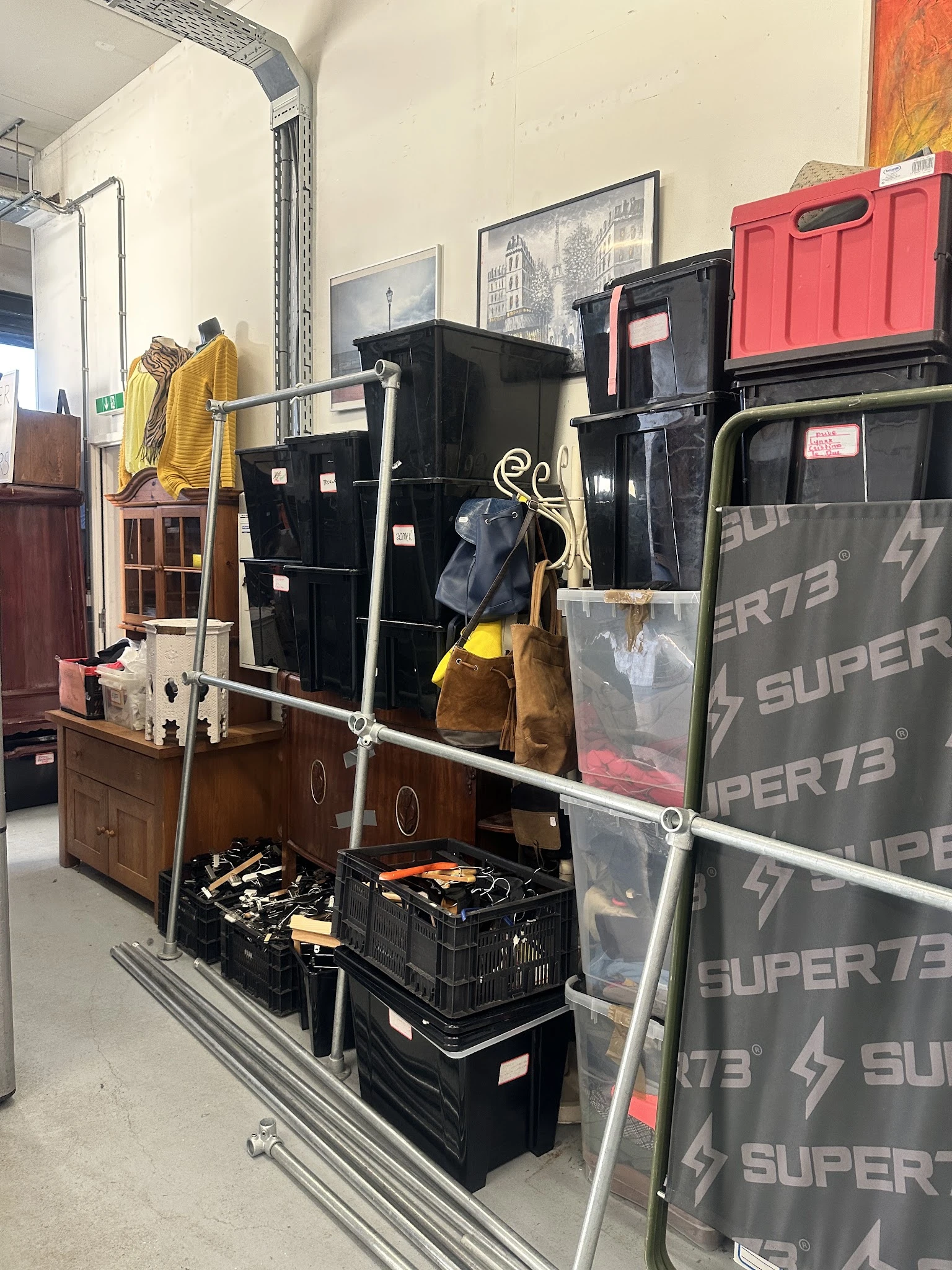 Uitgestalde tweedehands artikelen in de winkel: kleding op hangertjes, huishoudelijke spullen en boxen met diverse items