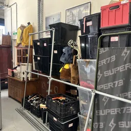 Uitgestalde tweedehands artikelen in de winkel: kleding op hangertjes, huishoudelijke spullen en boxen met diverse items