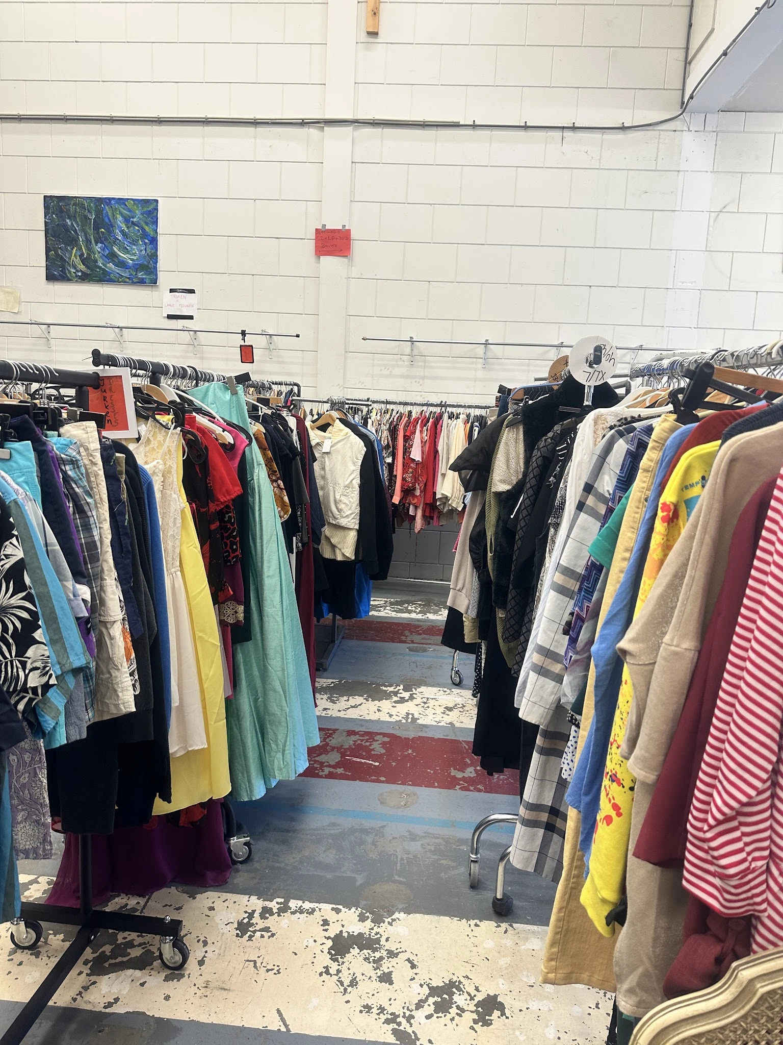 Rekken met tweedehands kleding in verschillende kleuren en stijlen in een kringloopwinkel