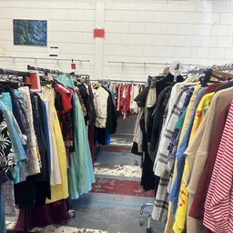 Rekken met tweedehands kleding in verschillende kleuren en stijlen in een kringloopwinkel