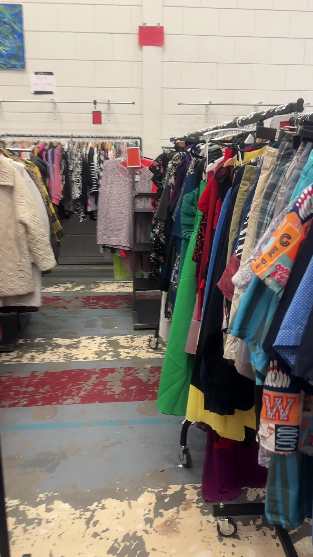 Rekken met tweedehands kleding in verschillende kleuren in de winkel