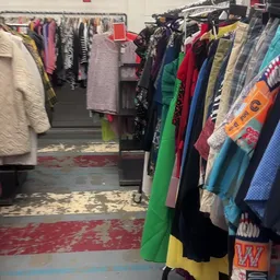 Rekken met tweedehands kleding in verschillende kleuren in de winkel
