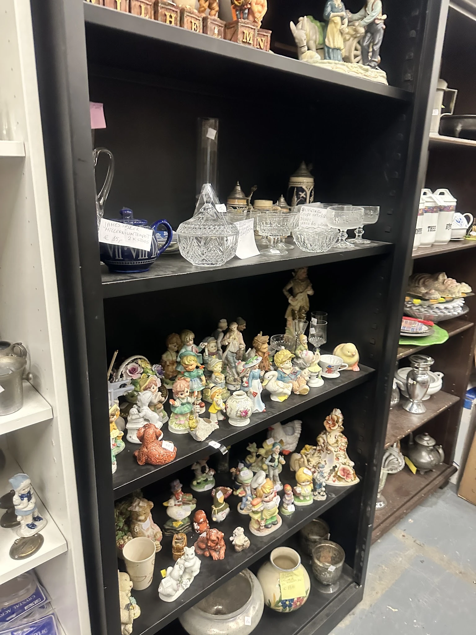 Zwarte kastenwand met verzameling decoratieve porseleinbeeldjes, kristallen glazen en andere secondhandsartikelen