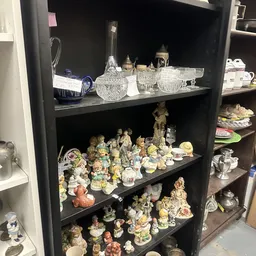 Zwarte kastenwand met verzameling decoratieve porseleinbeeldjes, kristallen glazen en andere secondhandsartikelen