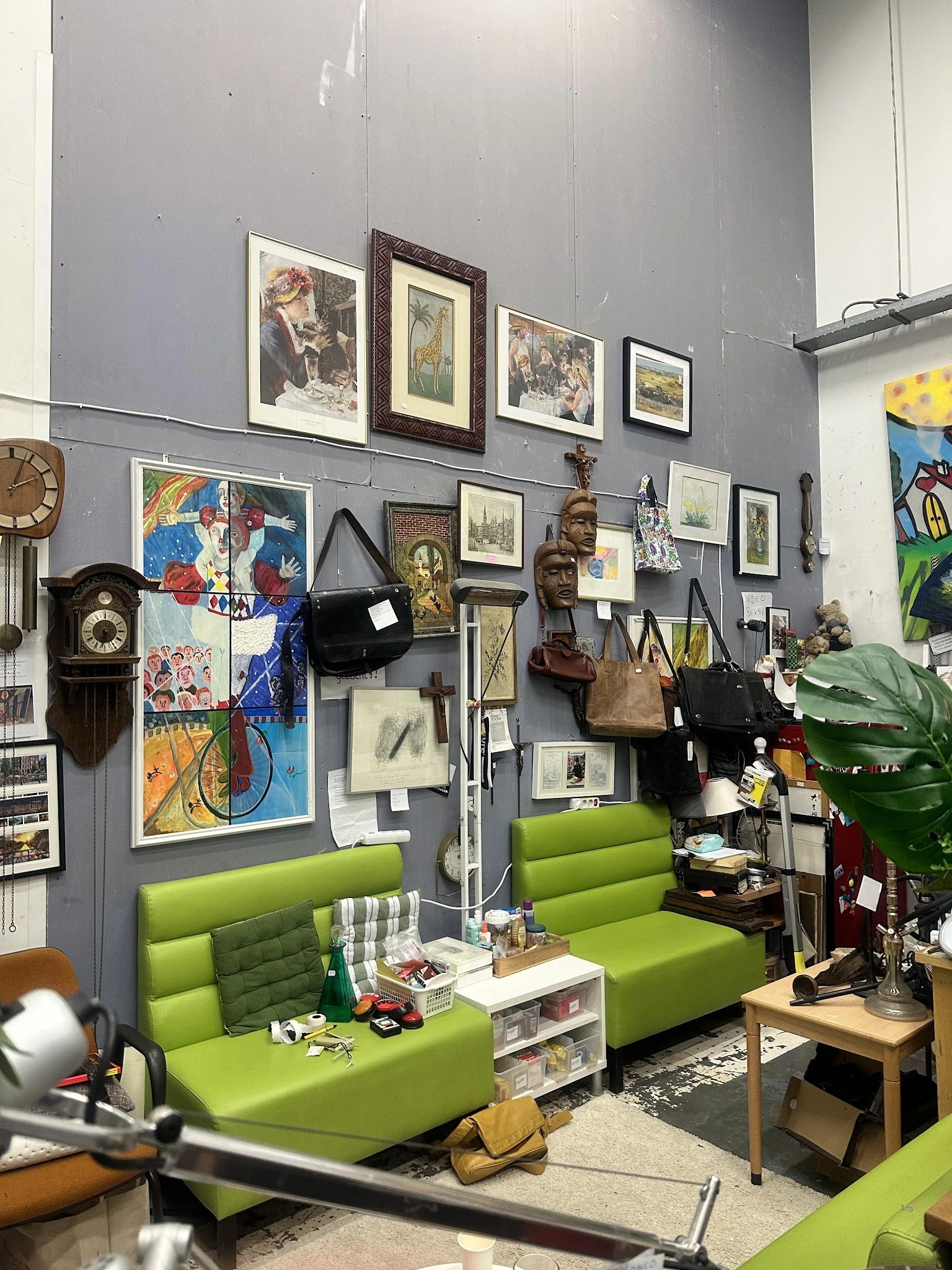 Winkelbinnenruimte met grijze wanden, groene banken en veel kunstwerken, prints en vintage voorwerpen aan de muren