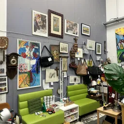 Winkelbinnenruimte met grijze wanden, groene banken en veel kunstwerken, prints en vintage voorwerpen aan de muren