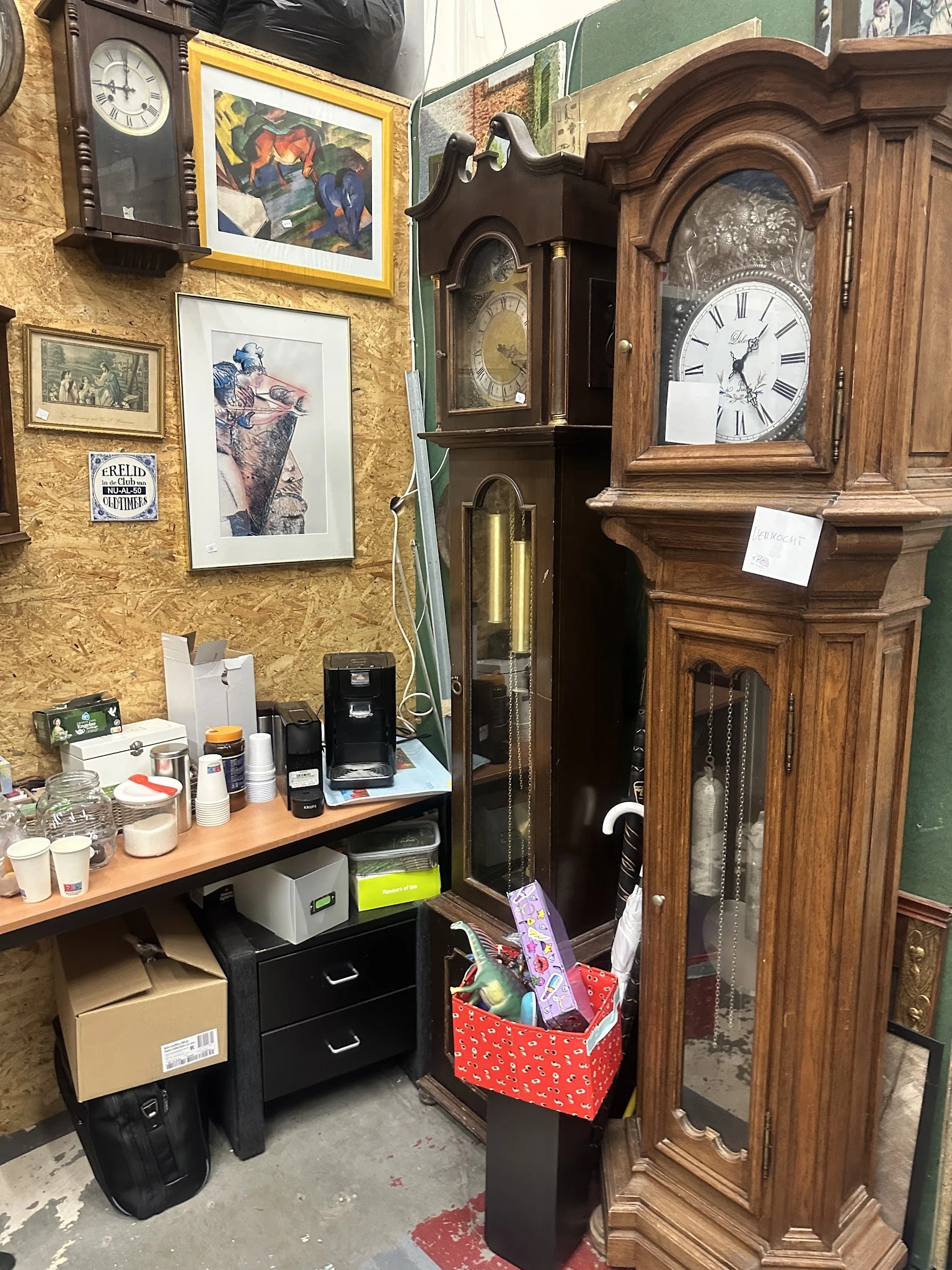 Hoek van winkelinterieur met werkplek, oude klok, kunstwerk aan geel behang en houten meubels