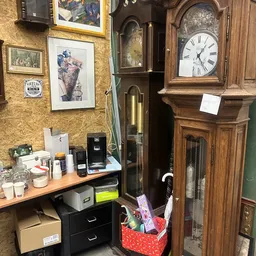 Hoek van winkelinterieur met werkplek, oude klok, kunstwerk aan geel behang en houten meubels