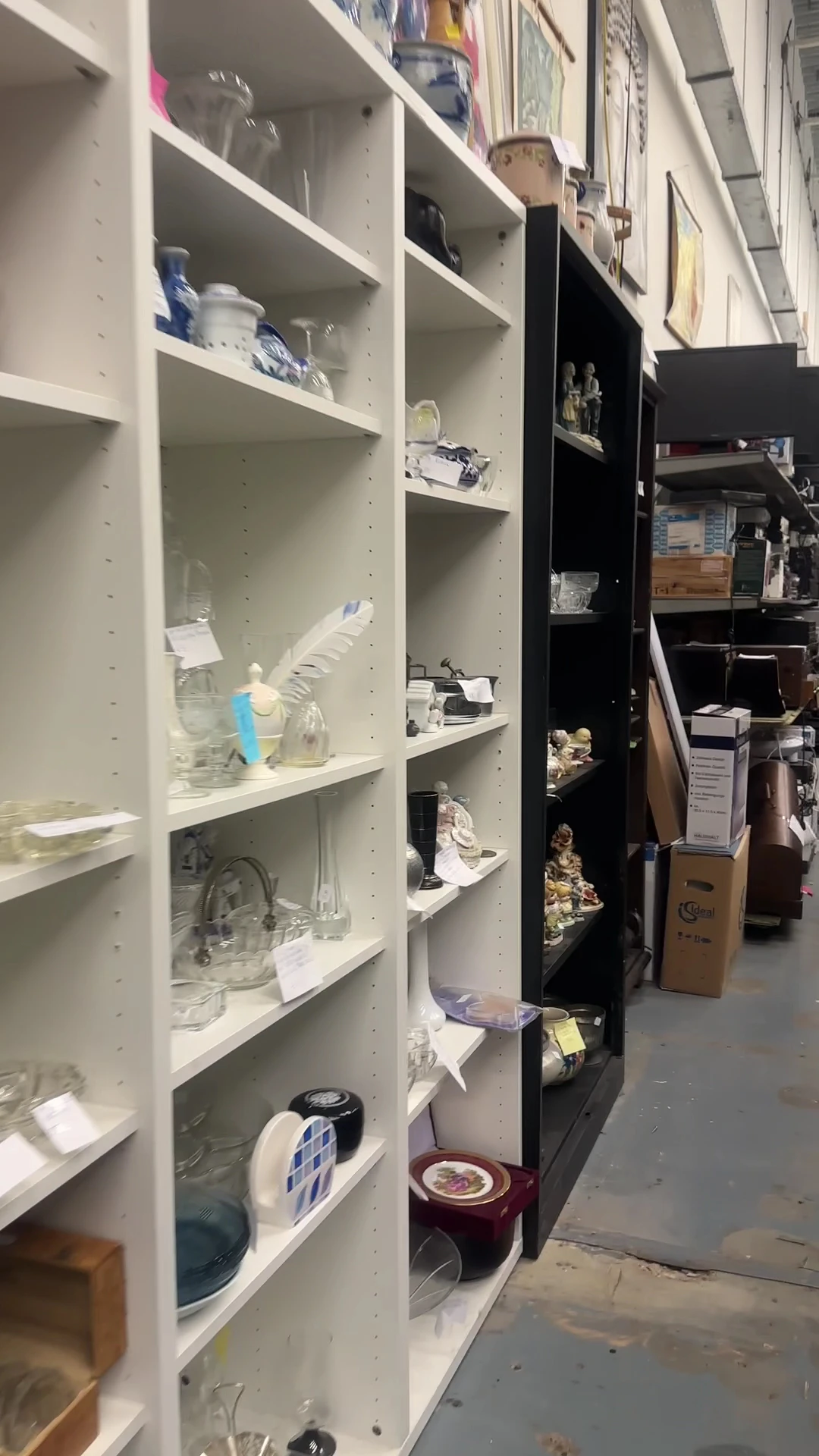 Witte en zwarte stellingen met diverse huishoudartikelen en glaswerk in een kringloopwinkel