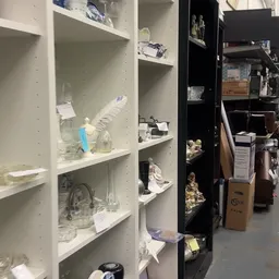 Witte en zwarte stellingen met diverse huishoudartikelen en glaswerk in een kringloopwinkel
