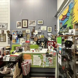 Winkelbinnenzicht met wanddecoratie, kunstwerk, boeken, huishoudartikelen en diverse tweedehands spullen op tafels en stellin