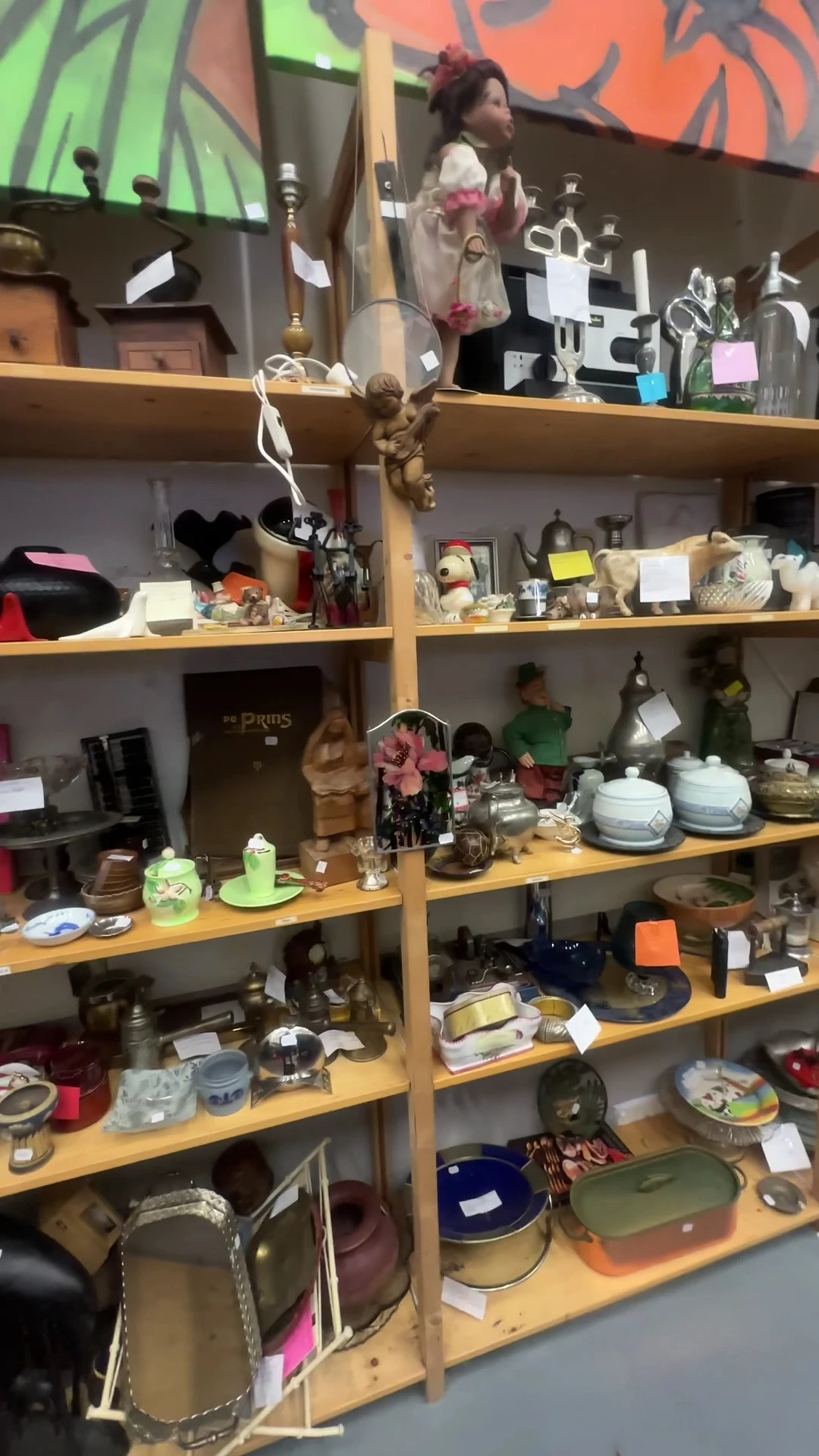Houten stellingen met diverse huishoudelijke artikelen, decoratie en serviesgoed in een kringloopwinkel
