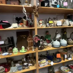 Houten stellingen met diverse huishoudelijke artikelen, decoratie en serviesgoed in een kringloopwinkel