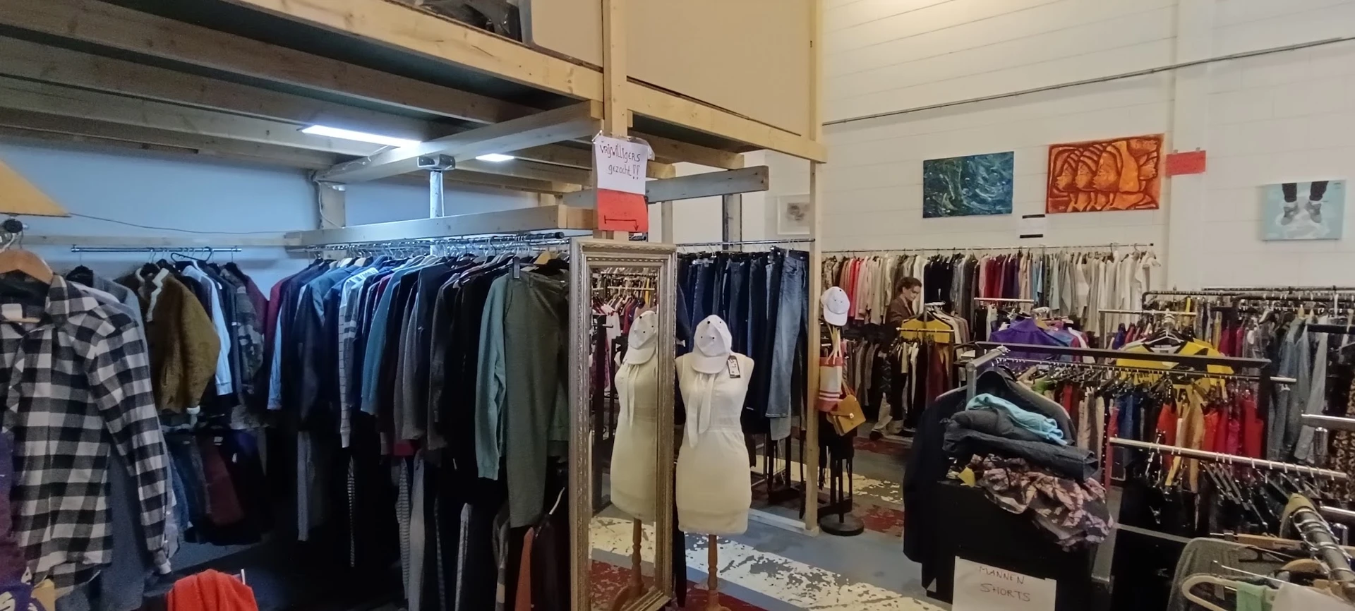 Rekken met tweedehands kleding in verschillende kleuren in de kringloopwinkel