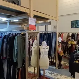 Rekken met tweedehands kleding in verschillende kleuren in de kringloopwinkel