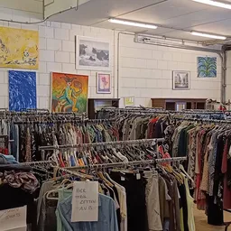 Rekken met tweedehands kleding en kunstwerken aan de muur in een kringloopwinkel