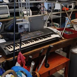 Elektronisch keyboard/synthesizer op houten tafel in werkruimte met muziekuitrusting op achtergrond