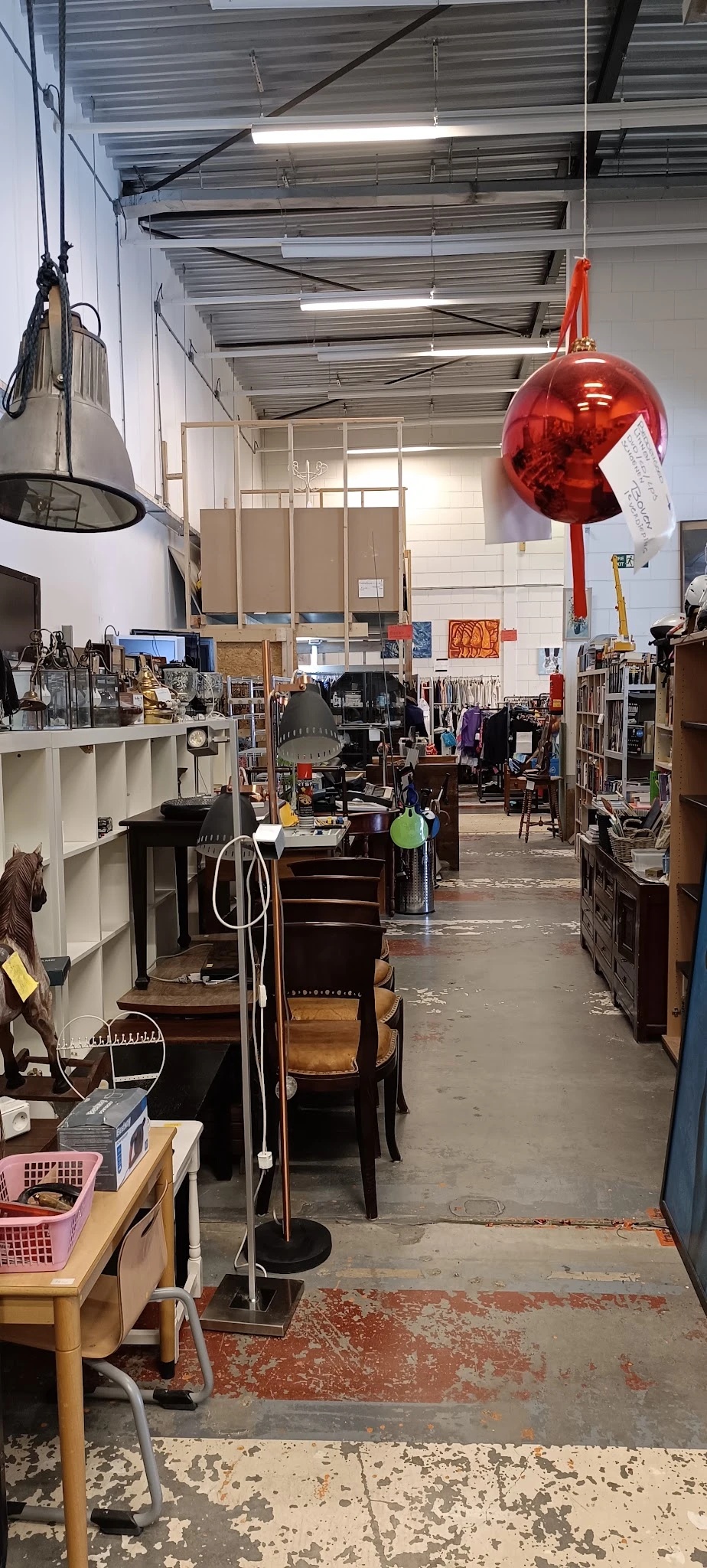 Binnenaanzicht van een kringloopwinkel met meubels, stellingen en diverse spullen verspreid over de vloer