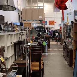 Binnenaanzicht van een kringloopwinkel met meubels, stellingen en diverse spullen verspreid over de vloer
