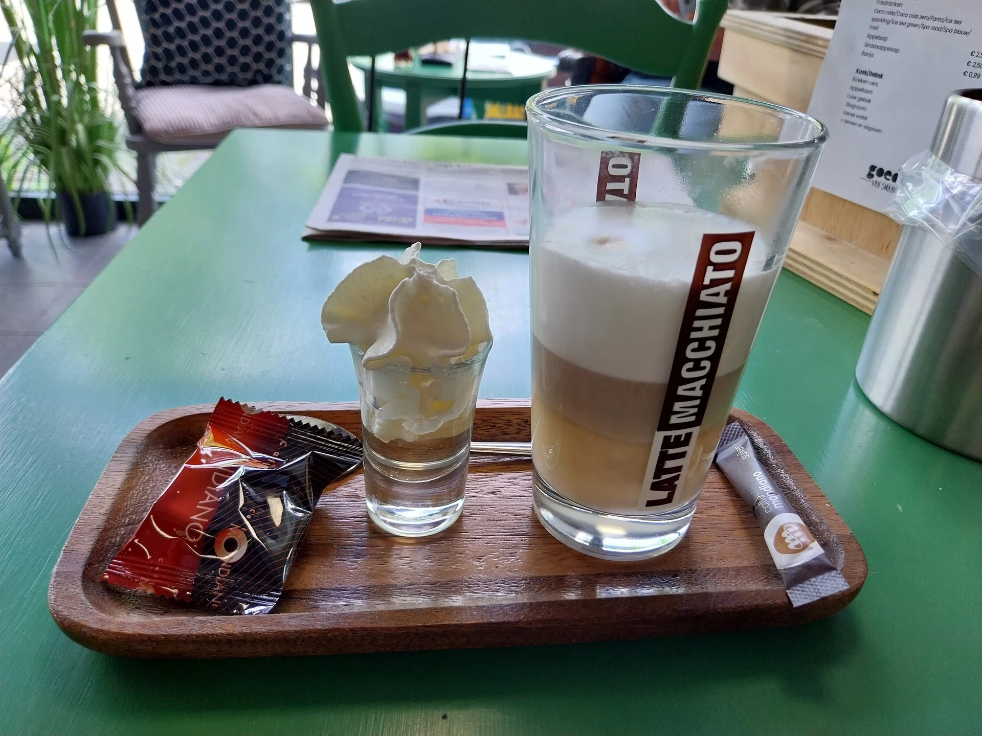 Twee glazen met frisdrank op een houten serveerplank met snacks, op groene tafel in lunchroom