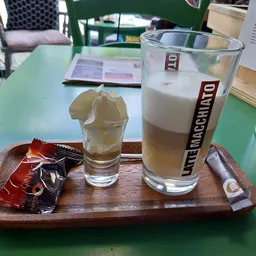 Twee glazen met frisdrank op een houten serveerplank met snacks, op groene tafel in lunchroom