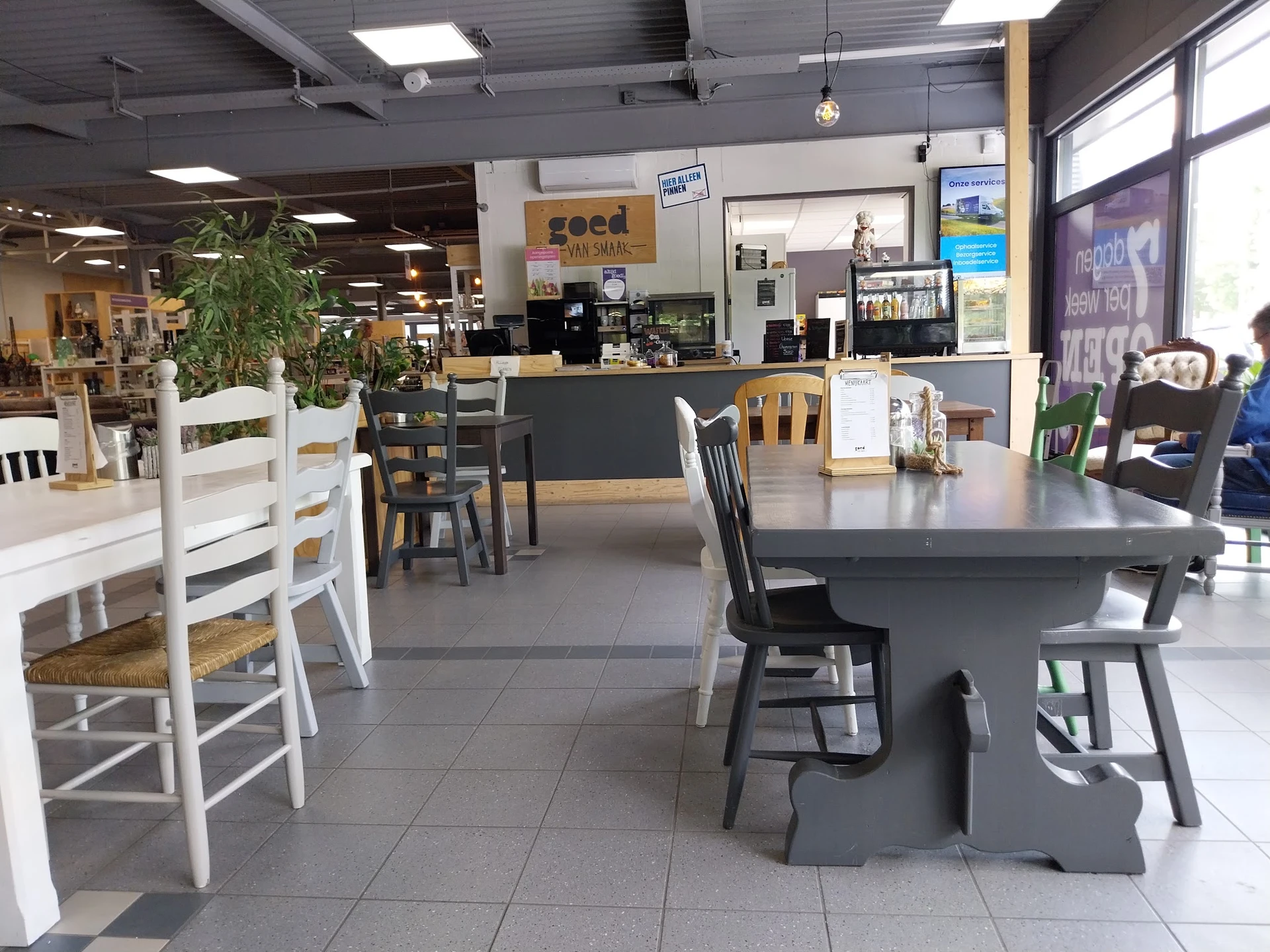 Winkelvloer met tafels en stoelen, kassazone op achtergrond, plantenbakken en stellingen