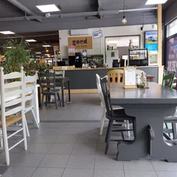 Winkelvloer met tafels en stoelen, kassazone op achtergrond, plantenbakken en stellingen