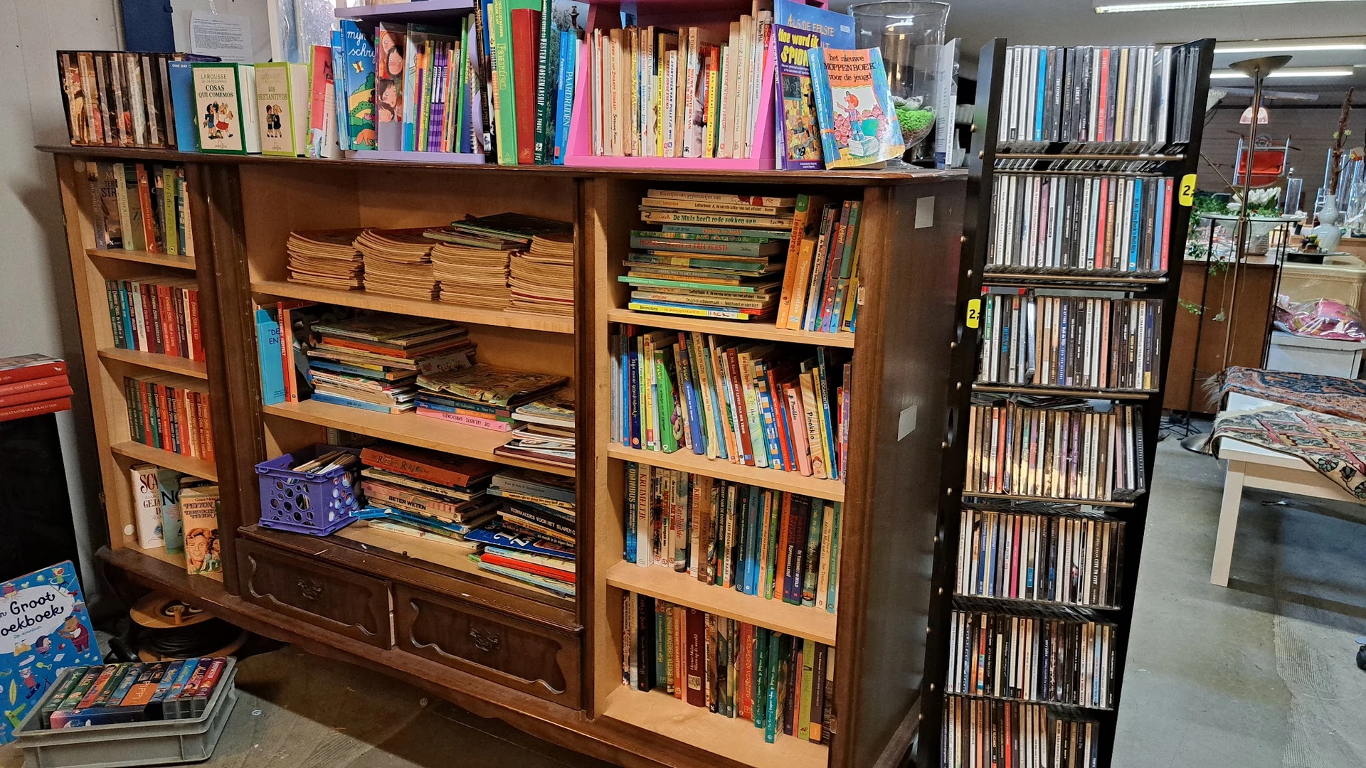 Houten boekenkast met verschillende secties vol met tweedehands boeken, dvd's en cd's netjes gerangschikt