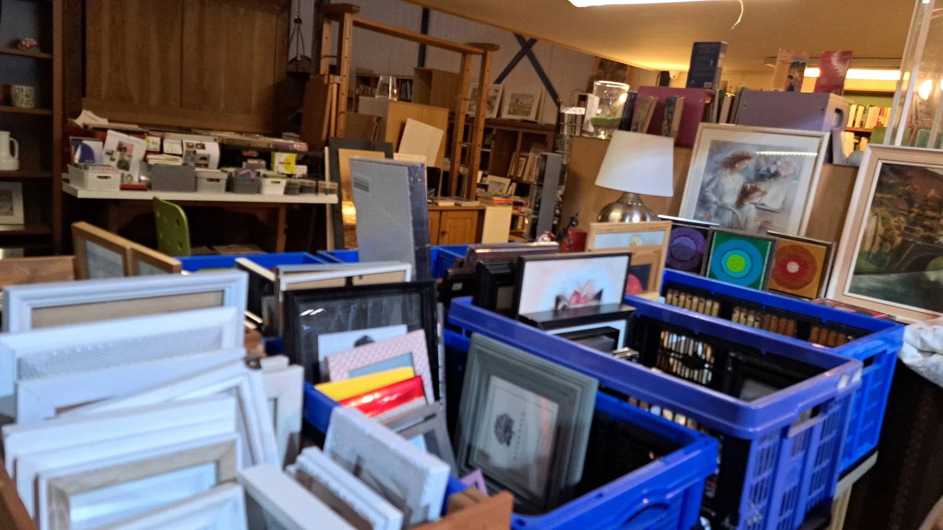 Blauwe kratjes met tweedehands items zoals frames, kunstwerken en diversen in een kringloopwinkel