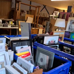 Blauwe kratjes met tweedehands items zoals frames, kunstwerken en diversen in een kringloopwinkel