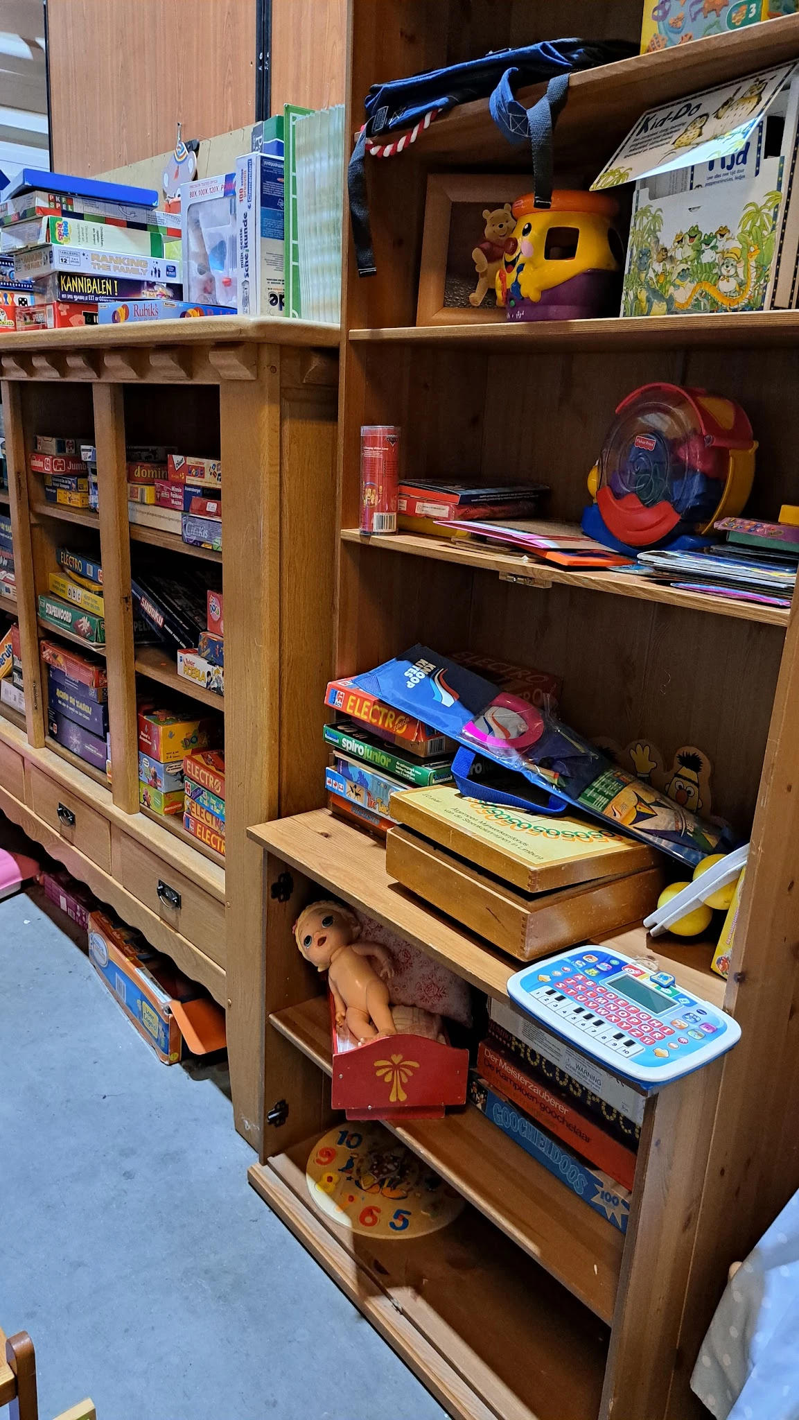 Houten kastje met verschillende items: gestapelde boeken, spelletjes, een pop, een frisbee en ander speelgoed