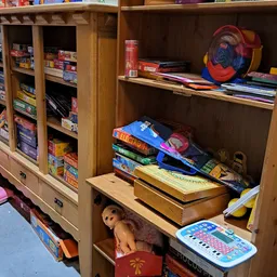 Houten kastje met verschillende items: gestapelde boeken, spelletjes, een pop, een frisbee en ander speelgoed
